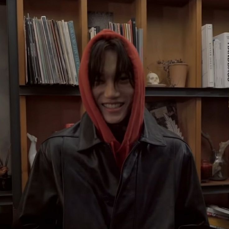 a person wearing a red hoodie in front of a bookshelf filled with records