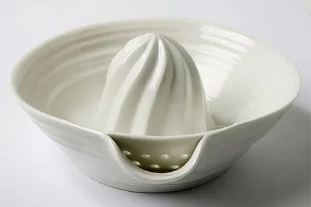 a white ceramic bowl with a large whisk in it's center, on a white surface