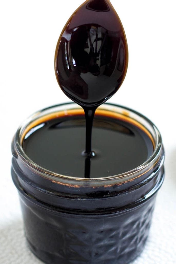 a spoon full of black liquid sitting on top of a table next to a jar