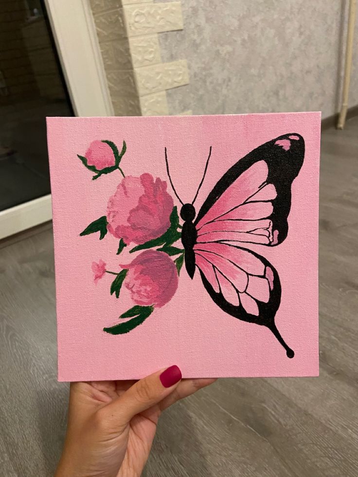 a hand holding up a pink card with a butterfly and flowers painted on the front