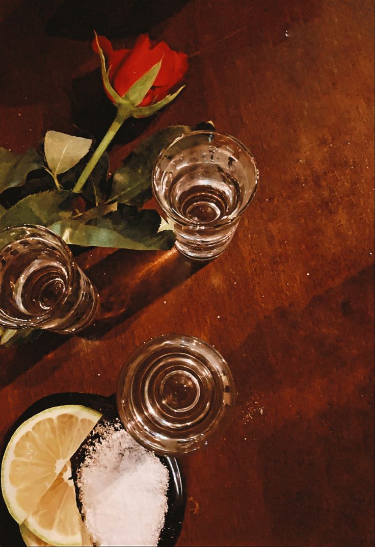 three shot glasses with salt and lemons on a wooden table next to a rose