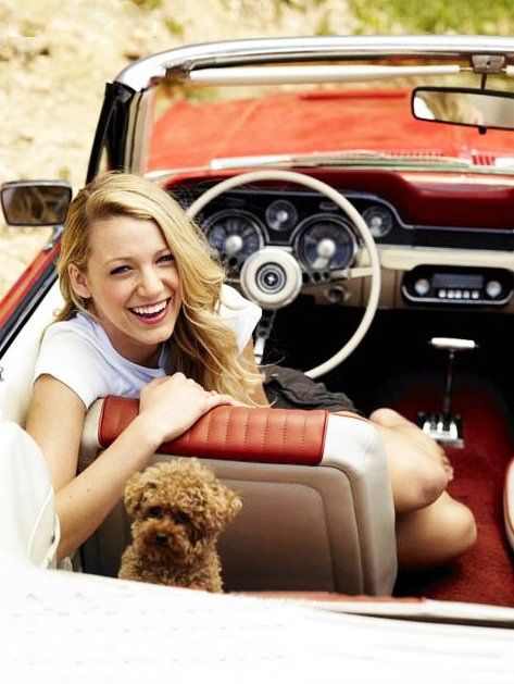 a woman sitting in the driver's seat of a convertible car with her dog