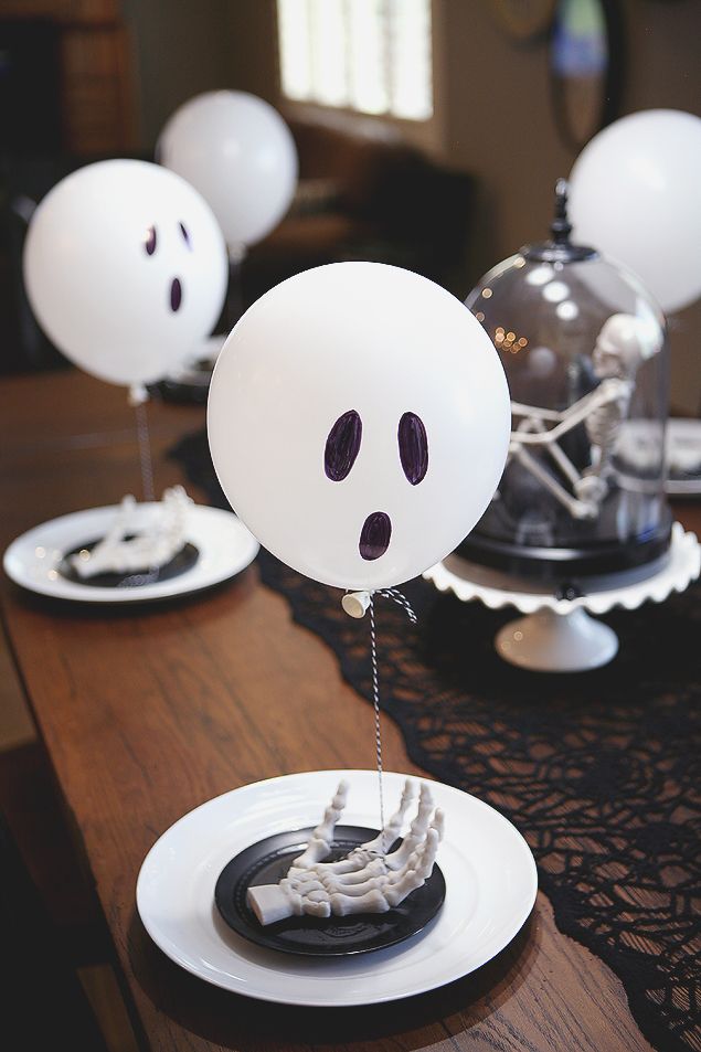 a table topped with plates and balloons decorated like ghost faces on top of each plate