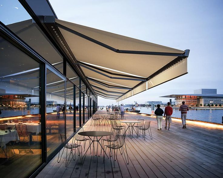 people are walking on the boardwalk next to an outdoor dining area with tables and chairs