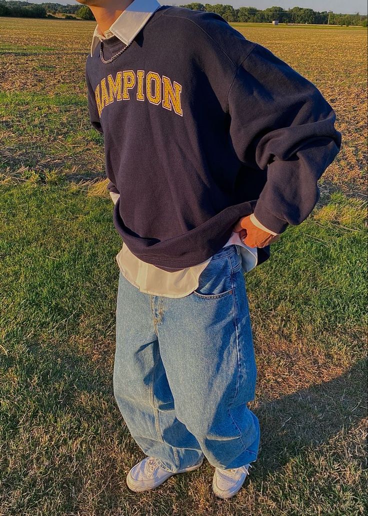 a young man standing in the middle of a field wearing a champion sweatshirt and jeans