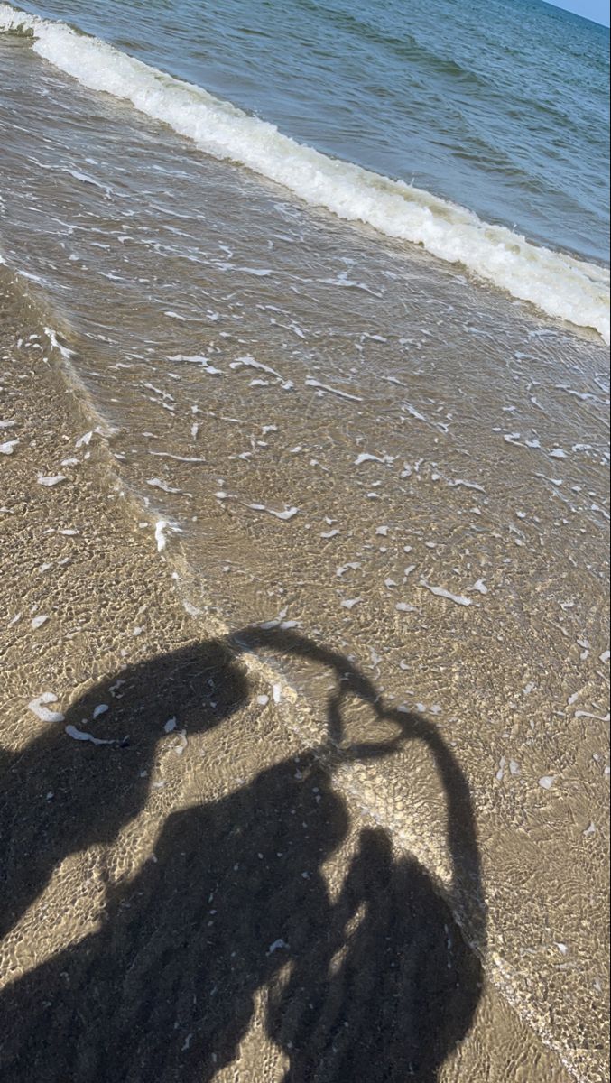 the shadow of a person riding a bike on the beach near the water's edge