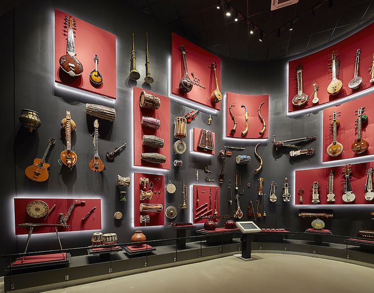 a display case filled with lots of musical instruments on red and black wall mounted shelves