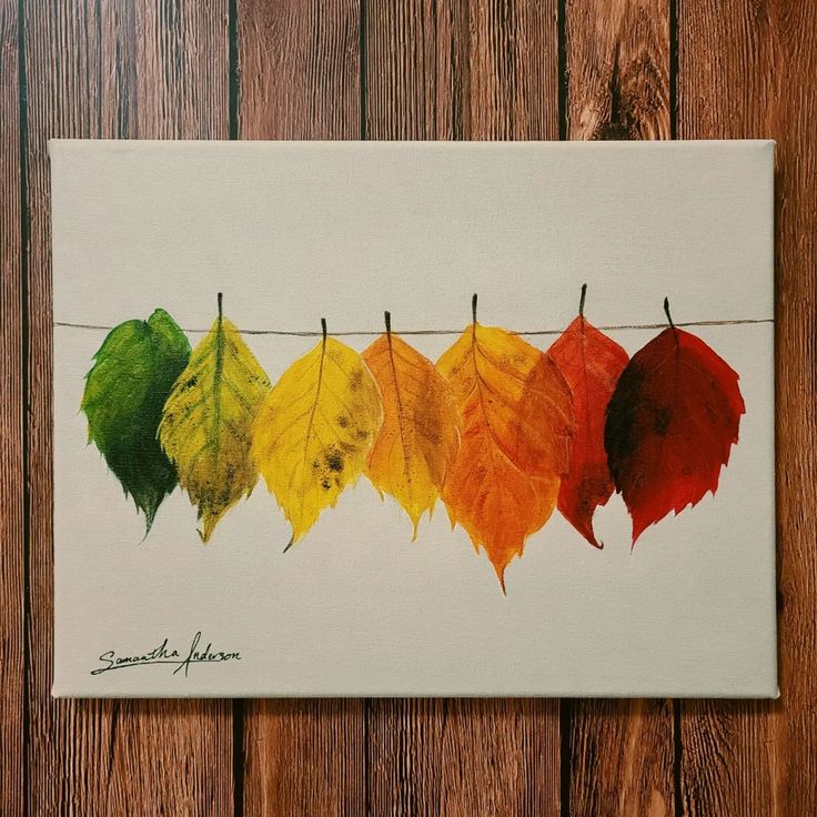 a painting of leaves hanging on a clothes line with the colors of autumn in them