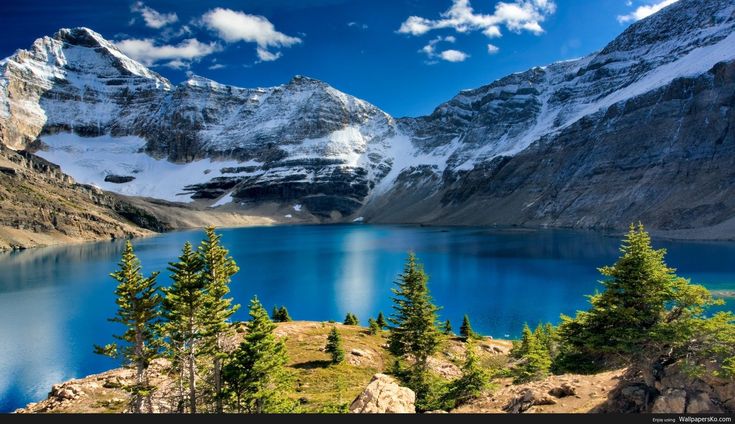 the mountains are covered in snow and blue water, with pine trees at the bottom