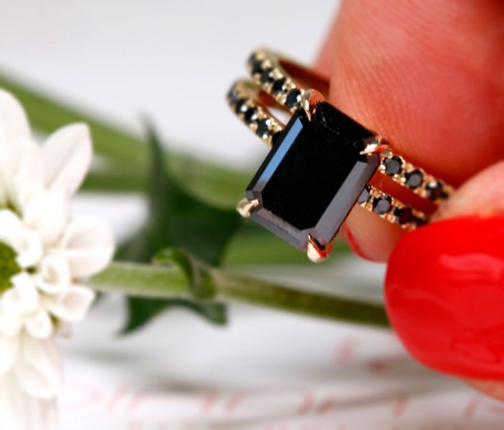 a close up of a person's hand holding a ring with a black stone on it