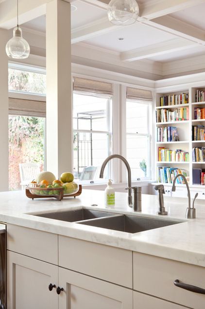 a kitchen with white cabinets and an island in front of a window that has bookshelves on it