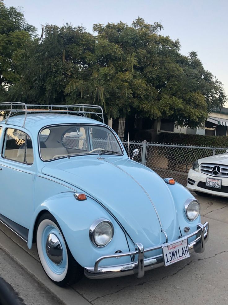 an old blue vw bug parked on the side of the road next to another car