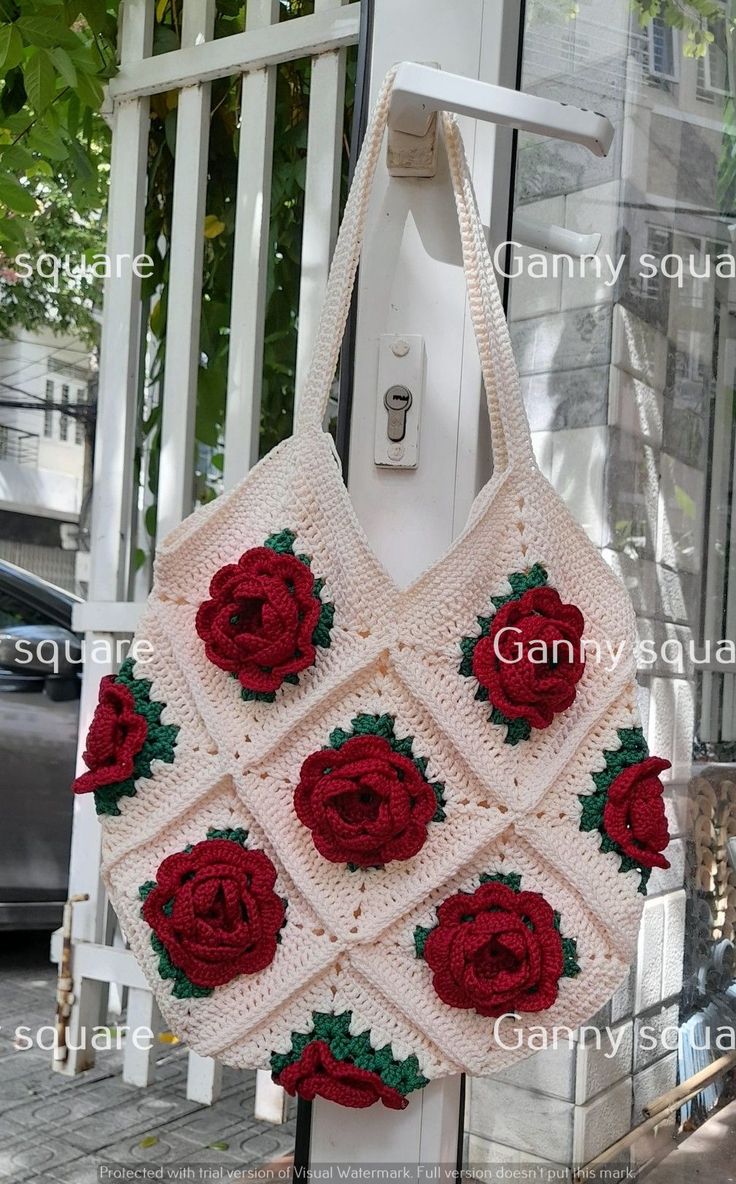 a crocheted bag with red roses hanging from it's side on a pole