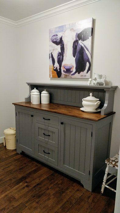 a kitchen with gray painted cabinets and wood flooring in the center, along with a cow painting on the wall