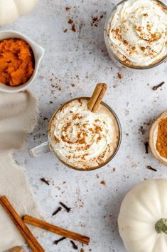 pumpkin spice lattes with whipped cream and cinnamon sticks on a white table top