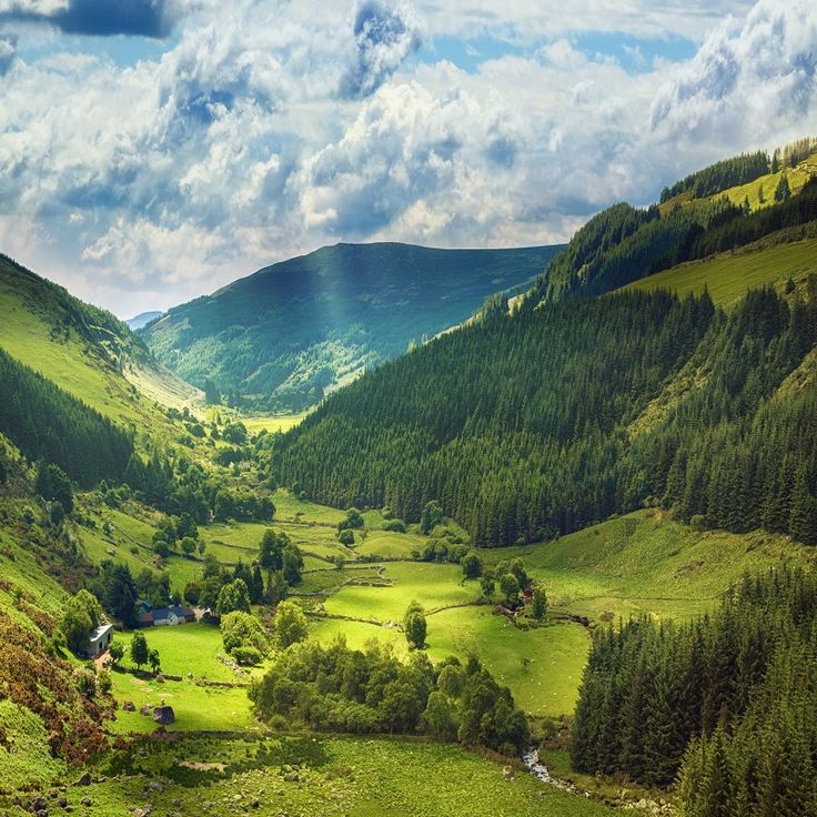 the valley is surrounded by green hills and trees, as well as clouds in the sky