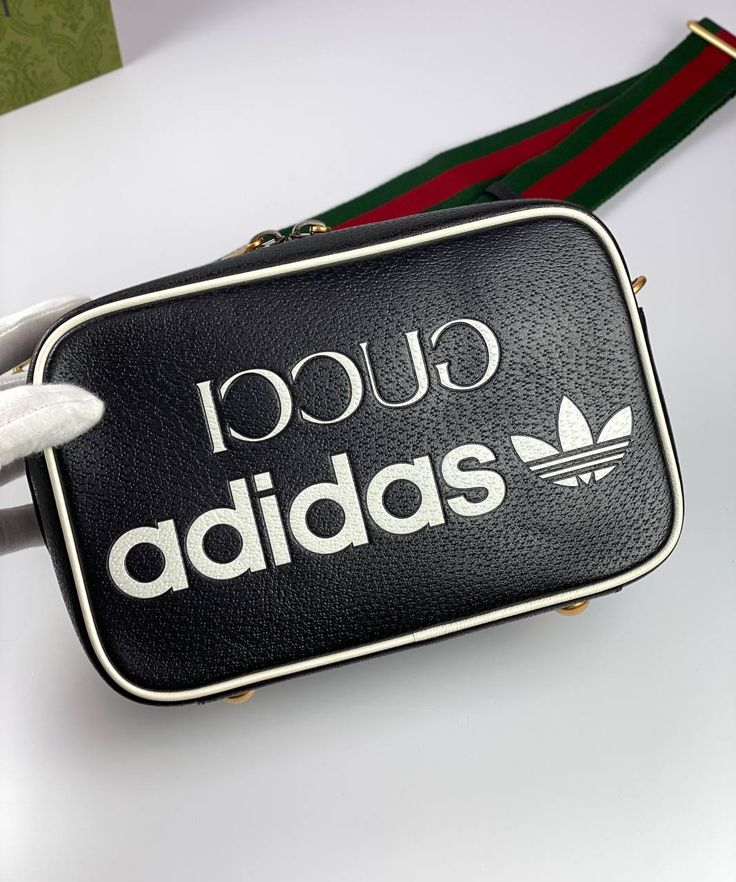 Part of the adidas x Gucci collection, this small shoulder bag features the 'Gucci adidas' and Trefoil print. adidas and Gucci venture into a collection, where the Web juxtaposes with the three white stripes, and the GG monogram combines with the trefoil. Pulling inspiration from the Creative Director’s memories of the '80s and '90s, emblematic House’s motifs mix with those of the historic sportswear brand adidas resulting in a series of hybrid looks. Adidas X Gucci, Gucci X Adidas, Gg Collection, Gucci Adidas, Gucci Collection, Gg Monogram, Adidas X, Shoulder Bag Black, Handbag Wallet