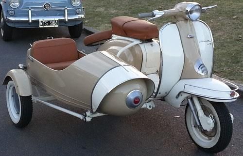 a scooter is parked on the side of the road next to an old car