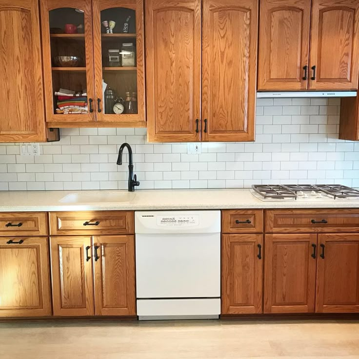 an empty kitchen with wooden cabinets and white tile backsplash, stove top oven and dishwasher