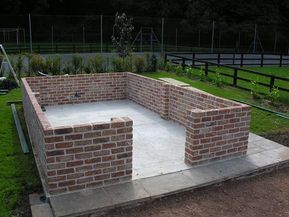 a brick fire pit sitting in the middle of a field next to a fence and grass