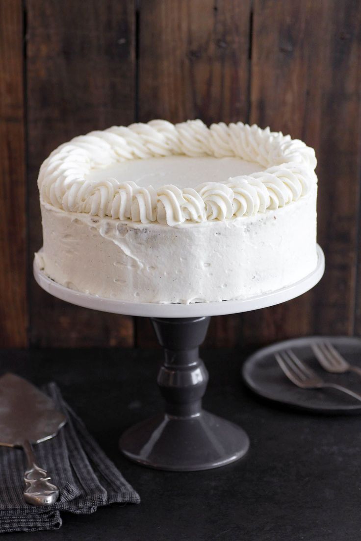 a white frosted cake sitting on top of a table next to a knife and fork