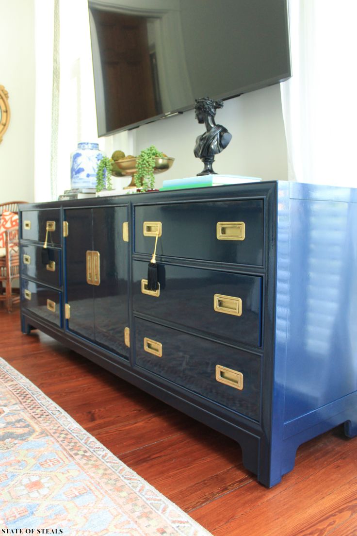 a blue dresser with gold handles and drawers in front of a flat screen tv mounted on the wall