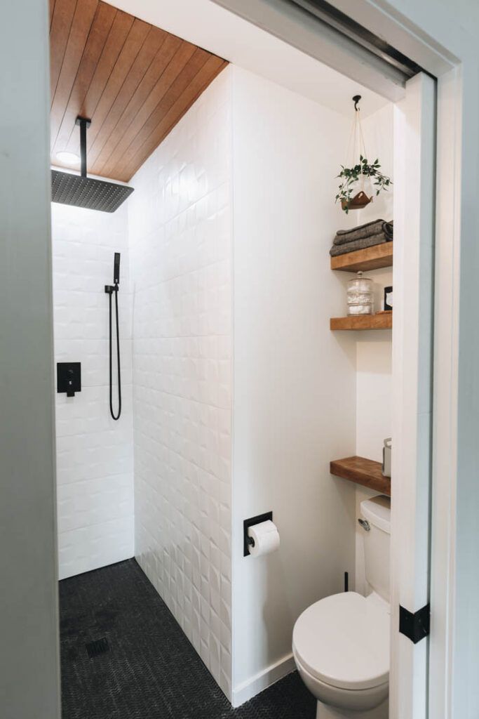 a white toilet sitting inside of a bathroom next to a walk in shower and wooden shelves