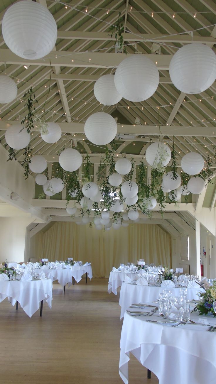 the ceiling is covered with paper lanterns and white tablecloths for an elegant wedding reception