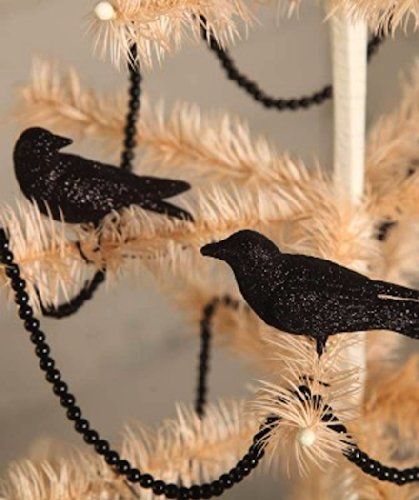 two black birds sitting on top of a white christmas tree with bead garland around it