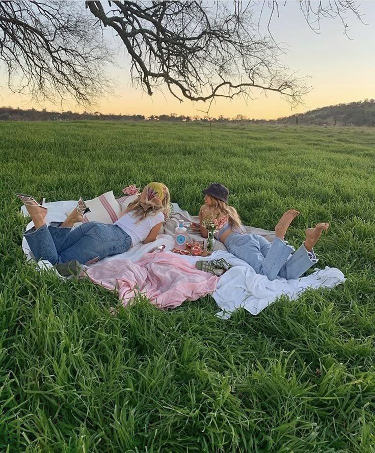 two women are laying in the grass and having a picnic