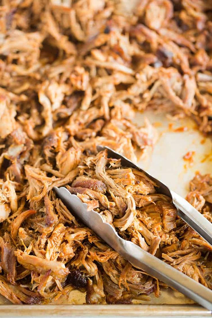 pulled pork in the oven on a baking sheet with tongs next to it and text overlay that reads pulled pork in the oven