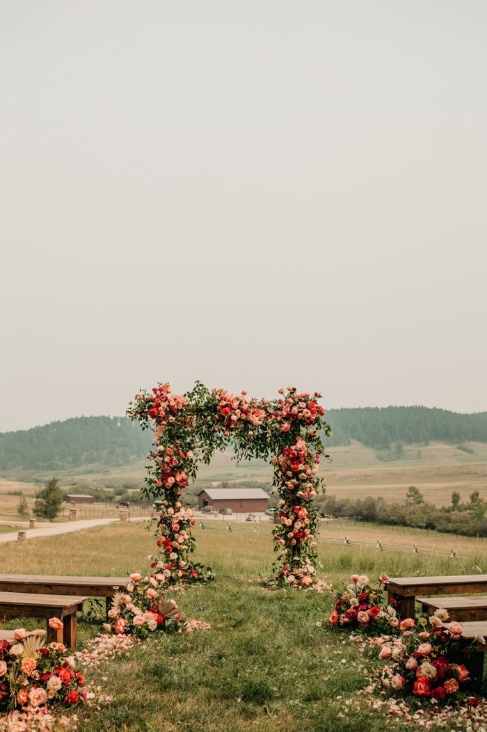 an outdoor ceremony setup with flowers and benches in the foreground, surrounded by rolling hills