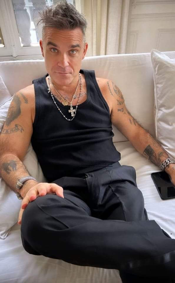 a man sitting on top of a white couch wearing black pants and a tank top