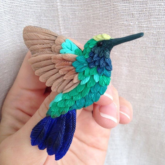 a hand holding a small bird made out of paper and colored feathers on it's wings