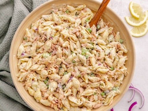 a wooden bowl filled with pasta salad next to sliced lemons