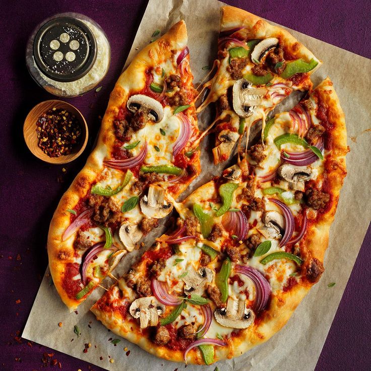 a pizza sitting on top of a table next to a bowl of seasoning and pepper