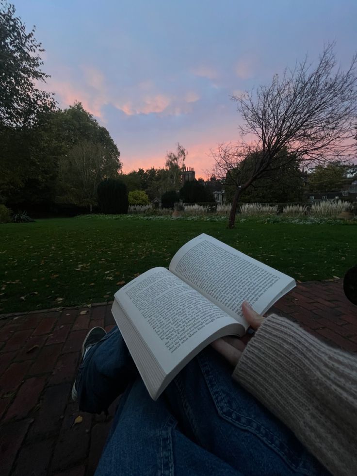 a person sitting on the ground holding an open book in their lap and reading it