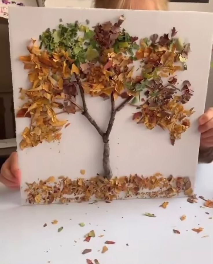 a child holding up a piece of paper that has a tree made out of leaves on it