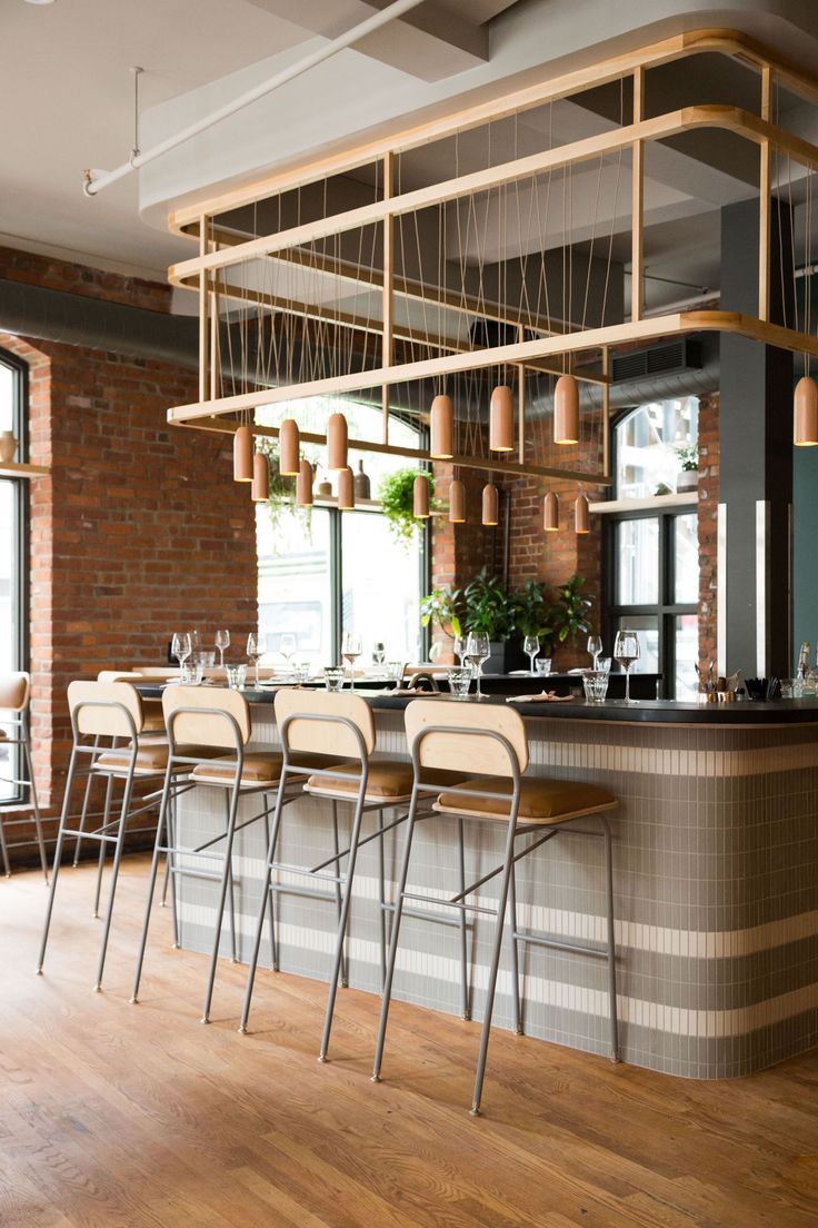 an empty bar with chairs and tables in front of large windows, next to a brick wall