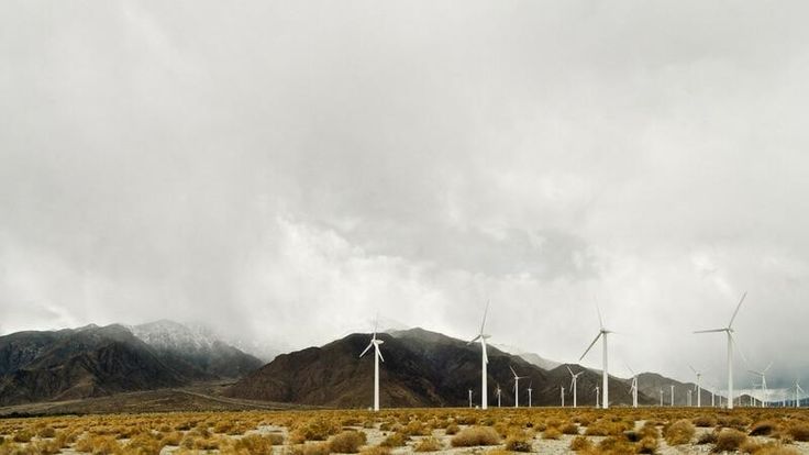 several wind mills in the desert with mountains in the background and cloudy skies above them