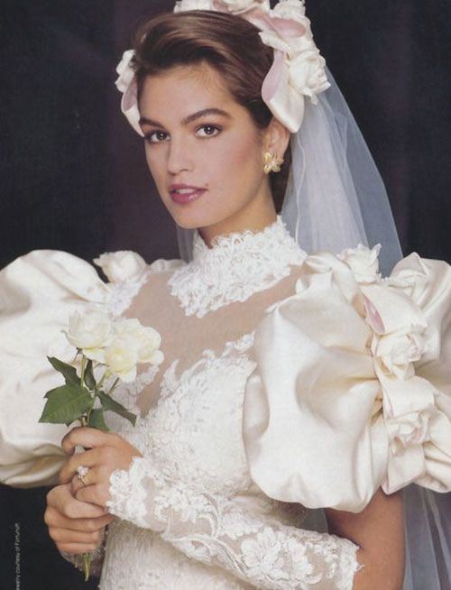 a woman wearing a wedding dress and holding a flower in her left hand while posing for the camera