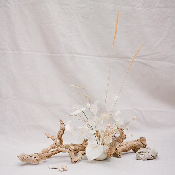 a vase filled with flowers sitting on top of a white table next to rocks and driftwood