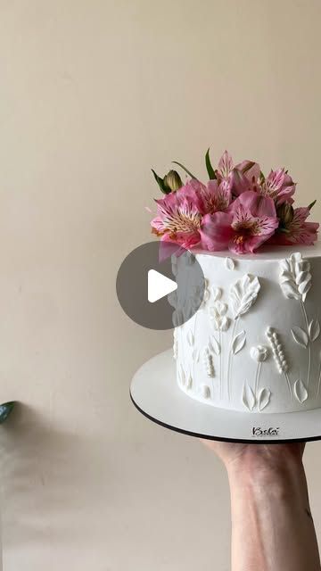 a person holding a white cake with pink flowers on top