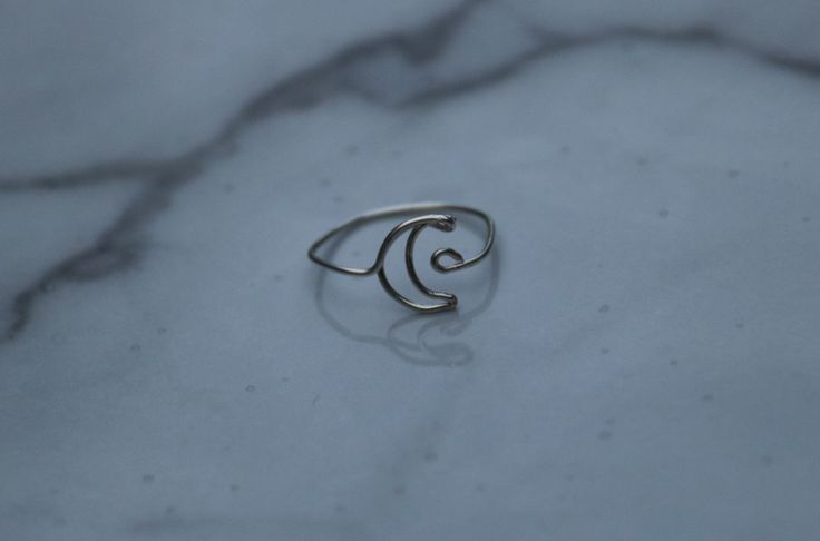 a silver ring sitting on top of a white marble surface with the letter c in it's middle