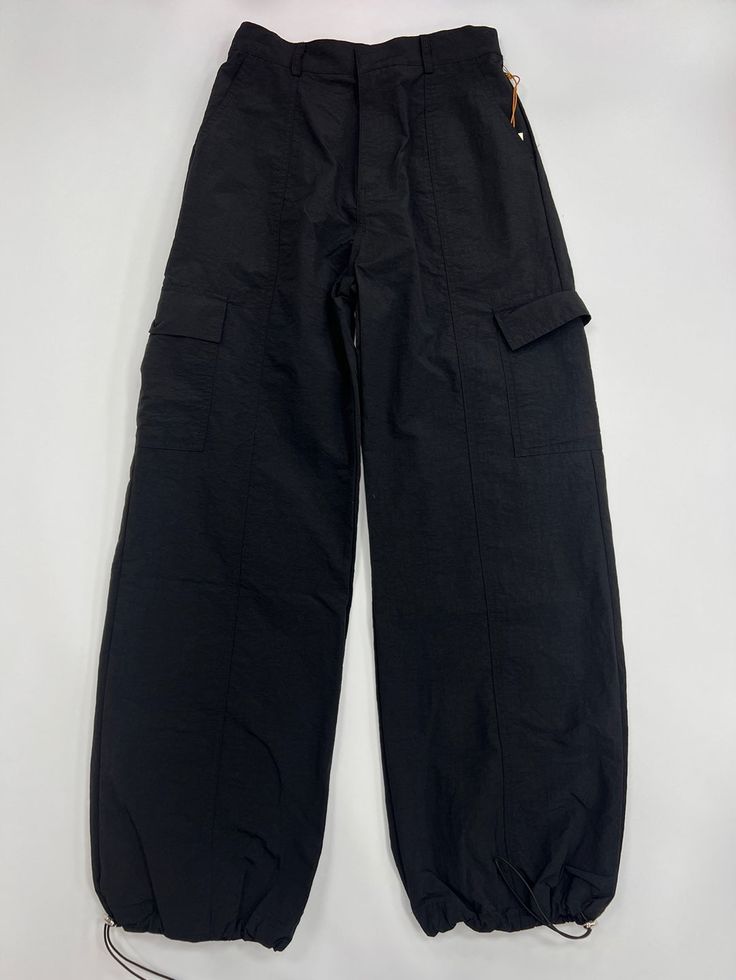 100% Nylon Loose Fit Pants Oversized Pockets on both legs Adjustable toggles at hem Baggy Solid Color Utility Parachute Pants, Solid Color Baggy Utility Parachute Pants, Baggy Solid Utility Parachute Pants, Baggy Bottoms With Elastic Waistband For Outdoor Activities, Utility Wide-leg Pants For Outdoor, Solid Color Drawstring Wide-leg Parachute Pants, High Waist Nylon Pants With Pockets, Casual Wide-leg Parachute Pants For Outdoor Activities, Wide Leg Nylon Parachute Pants With Drawstring