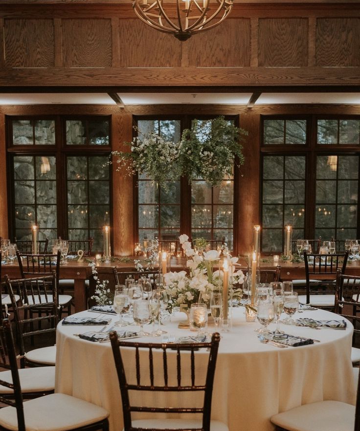 a table set up for a formal dinner with candles and flowers on the tables in front of large windows