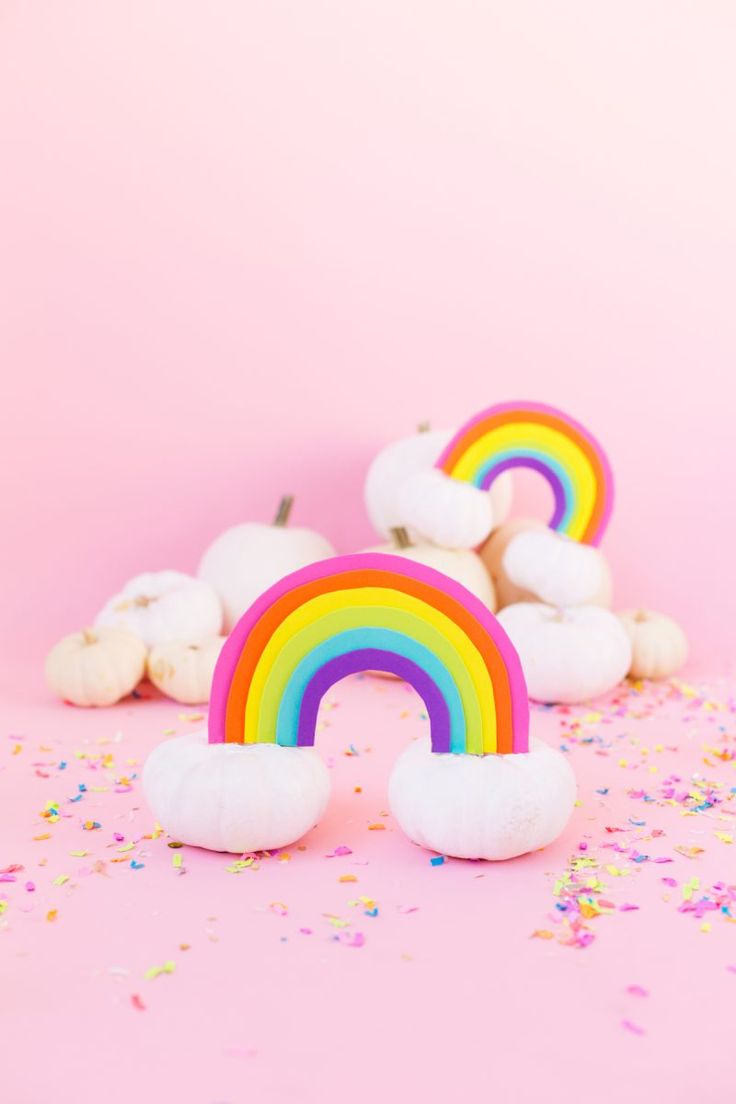 two rainbow shaped marshmallows on a pink background with sprinkles