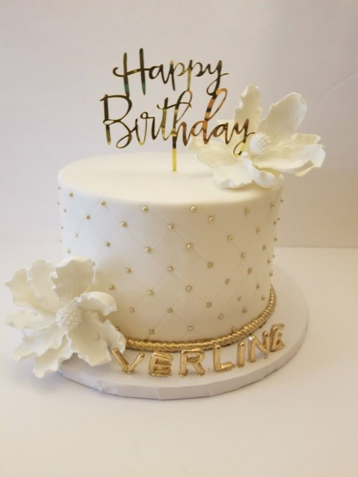 a white birthday cake with gold lettering and flowers