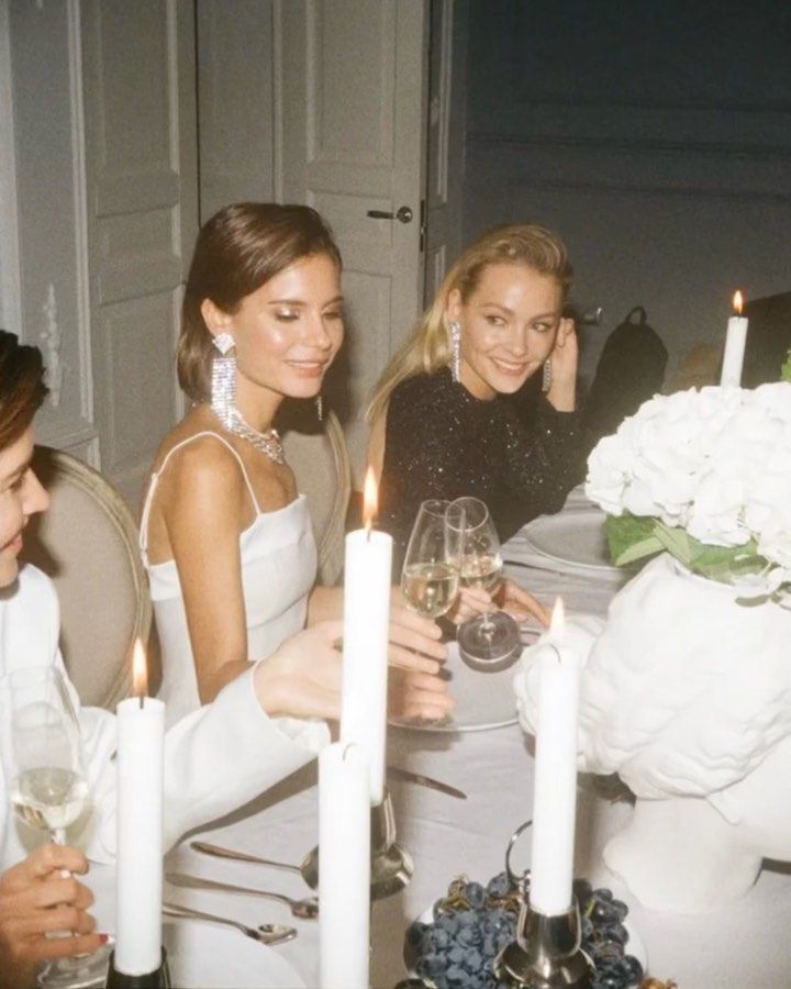 three women sitting at a table with wine glasses in front of them and candles on the table