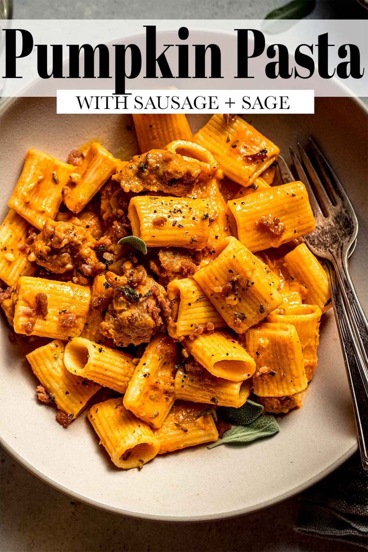 pumpkin pasta with sausage and sage in a white bowl next to a fork on a table